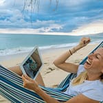 Frau in Hängematte am Strand mit Laptop ist stolz und freut sich über Nutzung von eBo