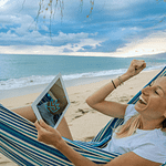 Frau in Hängematte am Strand mit Laptop ist stolz und freut sich über Nutzung von eBo
